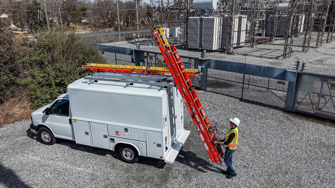 white box truck on job site with worker getting ladders off of a drop down ladder rack
