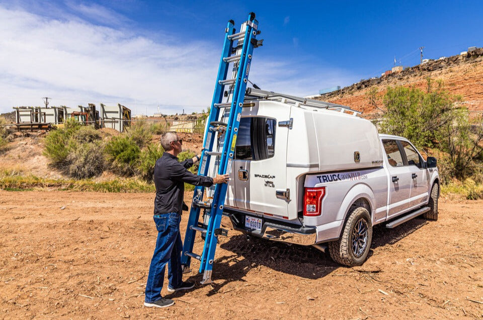 white work commercial fleet truck with topper cap and man loading drop down ladder rack